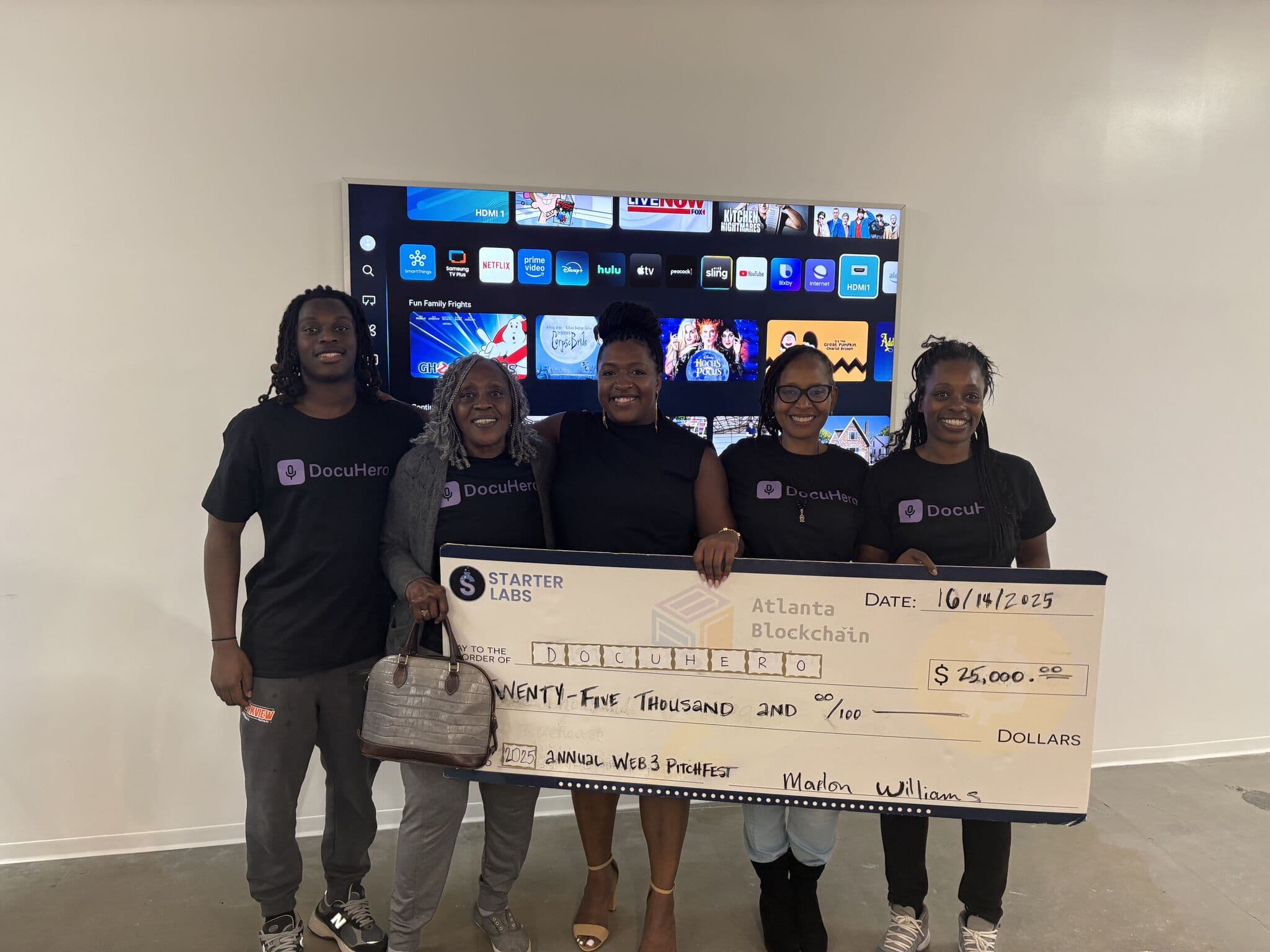 The DocuHero team in branded shirts, holding the $25,000 Pitchfest check